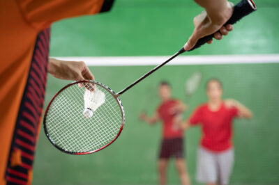 Badminton player holding a shuttlecock ready to serve with the opponent in a position ready to receive the shuttlecock when competing on the field